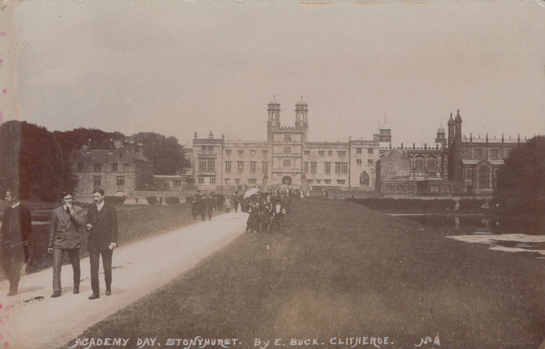 Vintage photograph of a large building with two men walking on a path in front.
