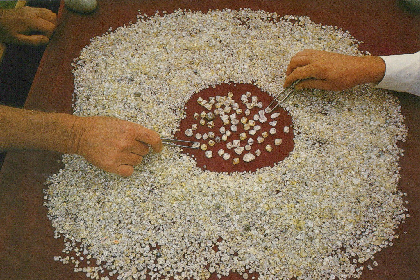 Hands sorting small stones on a red surface with a brown background
