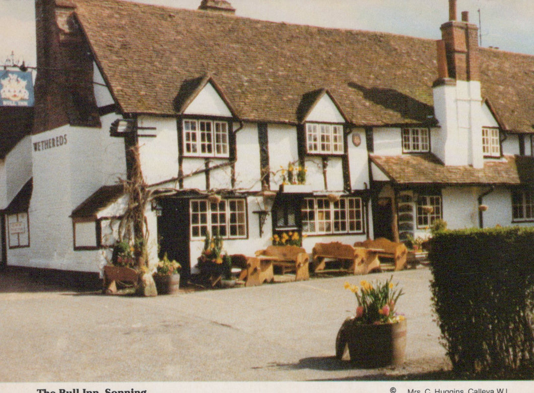 Traditional English pub with wooden benches and potted plants on a sunny day.