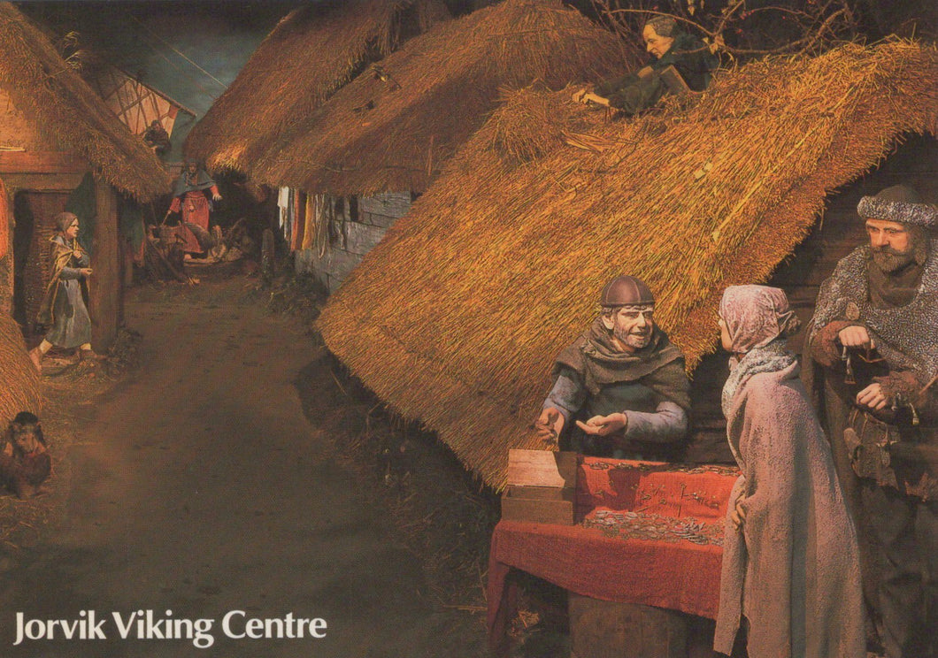 Viking scene with people around a table in a village setting, featuring thatched roofs and wooden huts.