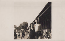 Load image into Gallery viewer, Two people standing on a beach with a building and other people in the background.
