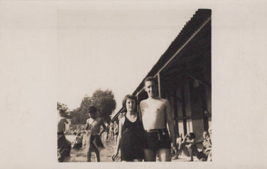 Two people standing on a beach with a building and other people in the background.