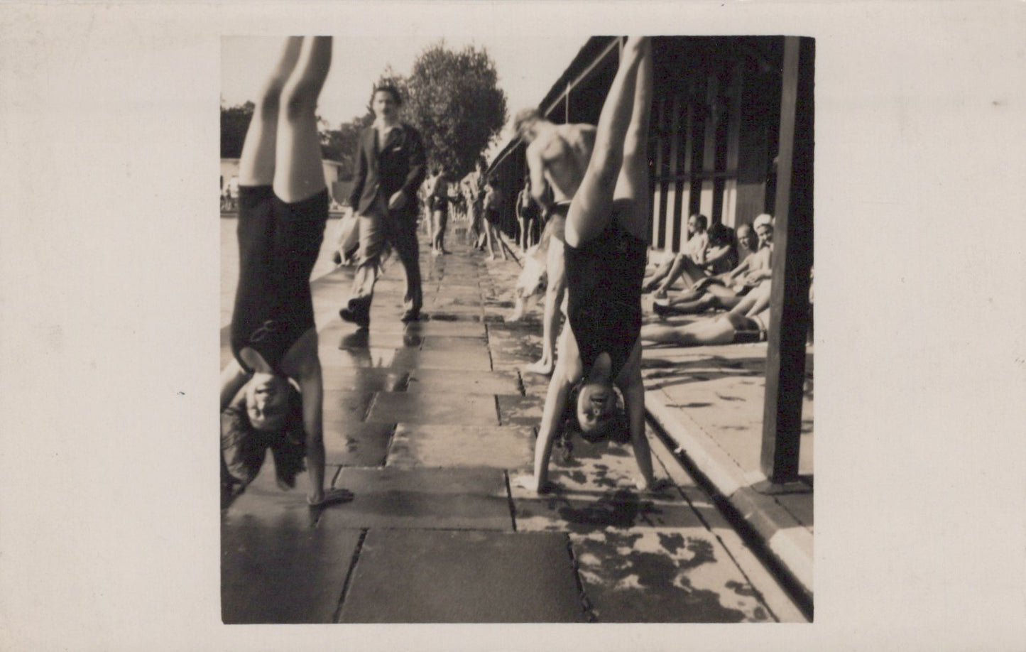 Two people doing handstands on a wooden deck with other people in the background.