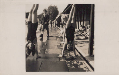 Two people doing handstands on a wooden deck with other people in the background.