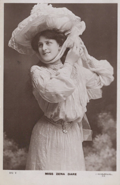 Vintage black and white photograph of a woman in an elaborate dress and hat, with a blurred background.