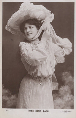 Vintage black and white photograph of a woman in an elaborate dress and hat, with a blurred background.