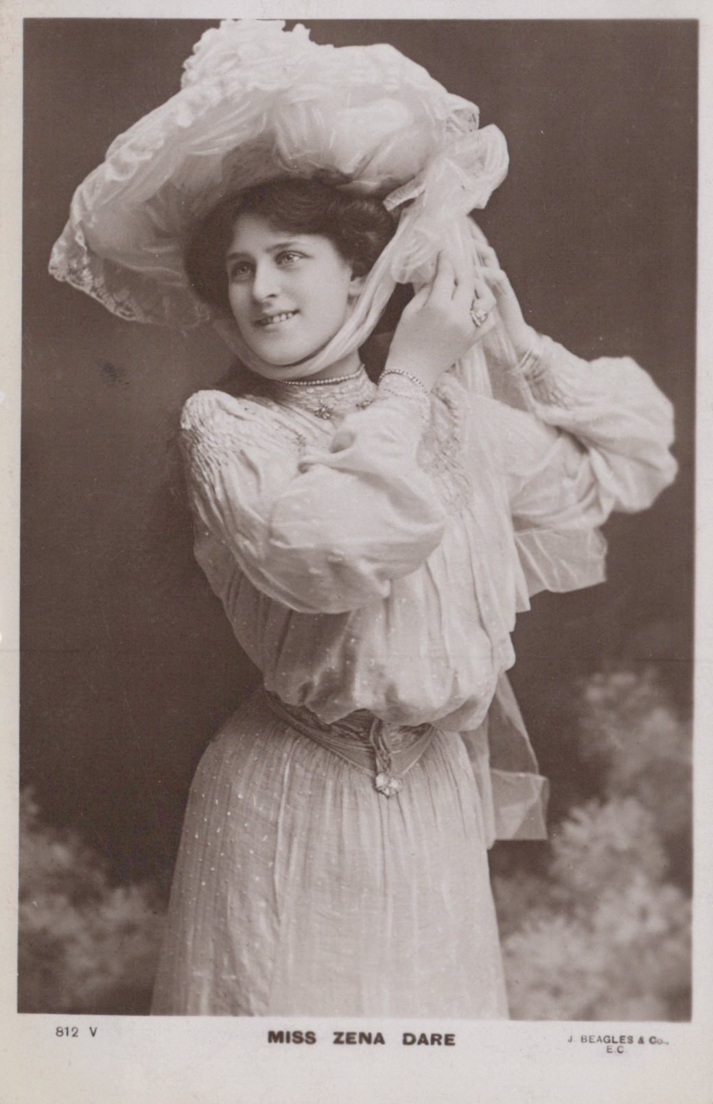 Vintage black and white photograph of a woman in an elaborate dress and hat, with a blurred background.