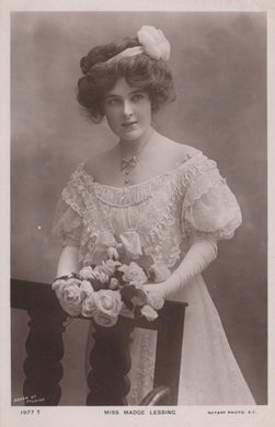 Vintage black and white portrait of a woman holding flowers, wearing an ornate dress and hat.