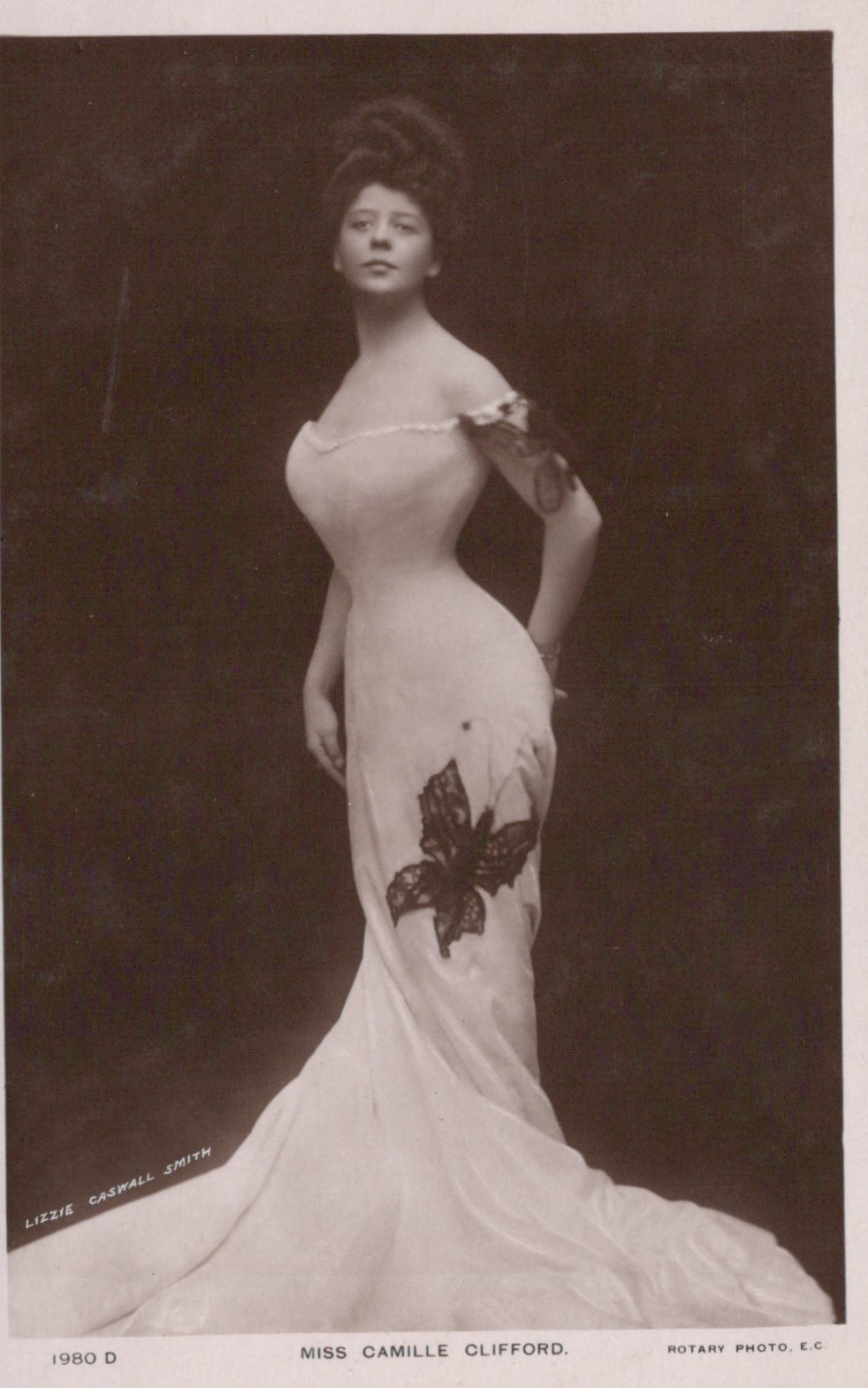 Vintage photograph of a woman in an elegant gown with a butterfly design, against a dark background.