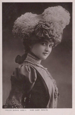 Vintage black and white portrait of a woman wearing an elaborate hat with feathers and flowers.