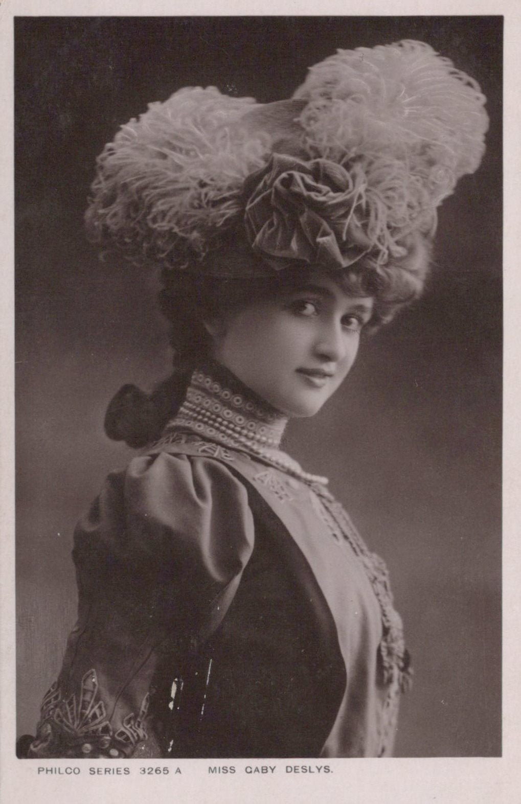 Vintage black and white portrait of a woman wearing an elaborate hat with feathers and flowers.