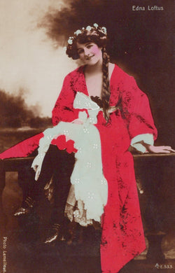 Woman in a red dress with white accents sitting outdoors, wearing a floral headpiece.