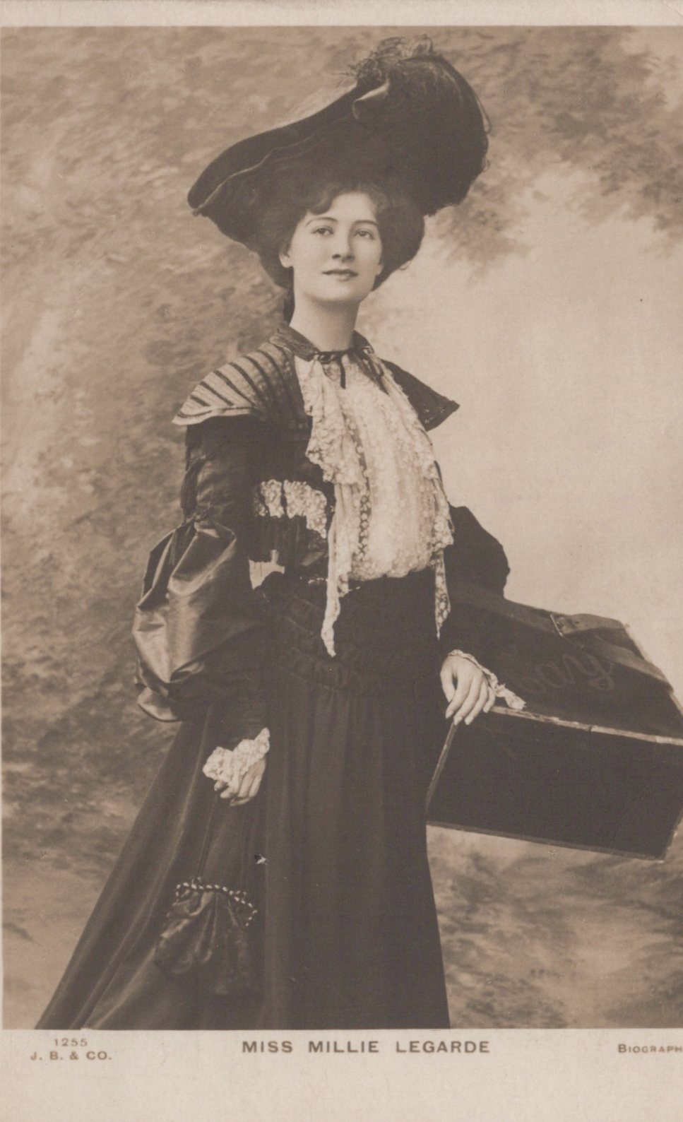 Vintage photograph of a woman in formal attire with a large hat and a fan, against a plain background.