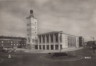 Vintage black and white photo of a large building with a clock tower and surrounding street scene.