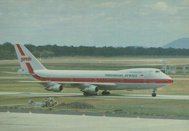 Indonesian Airways airplane on a runway with trees and mountains in the background