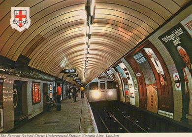 Underground station with curved ceiling and people waiting, featuring the London Underground logo.