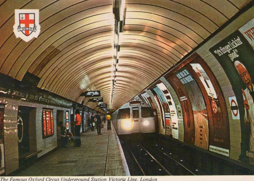 Underground station with curved ceiling and people waiting, featuring the London Underground logo.