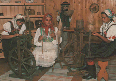 Three women in traditional attire using spinning wheels in a wooden room.