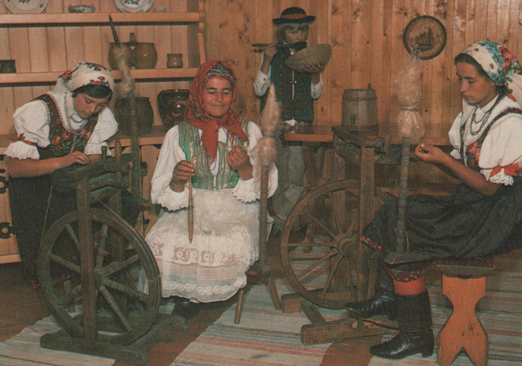 Three women in traditional attire using spinning wheels in a wooden room.