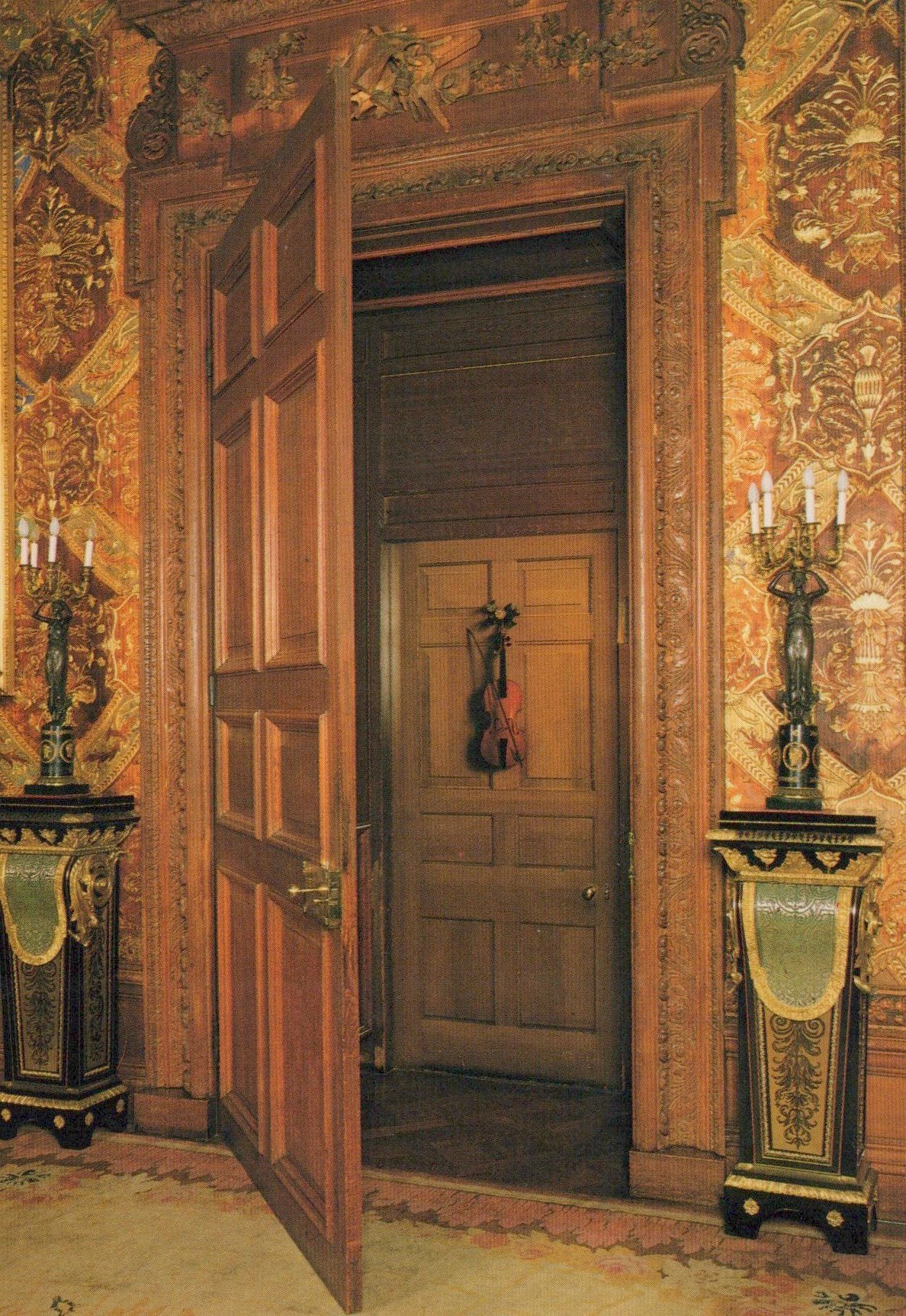 Decorative interior with open wooden door, ornate walls, and candle holders.