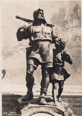 Black and white statue of a man with a child on his shoulders, with a castle in the background.