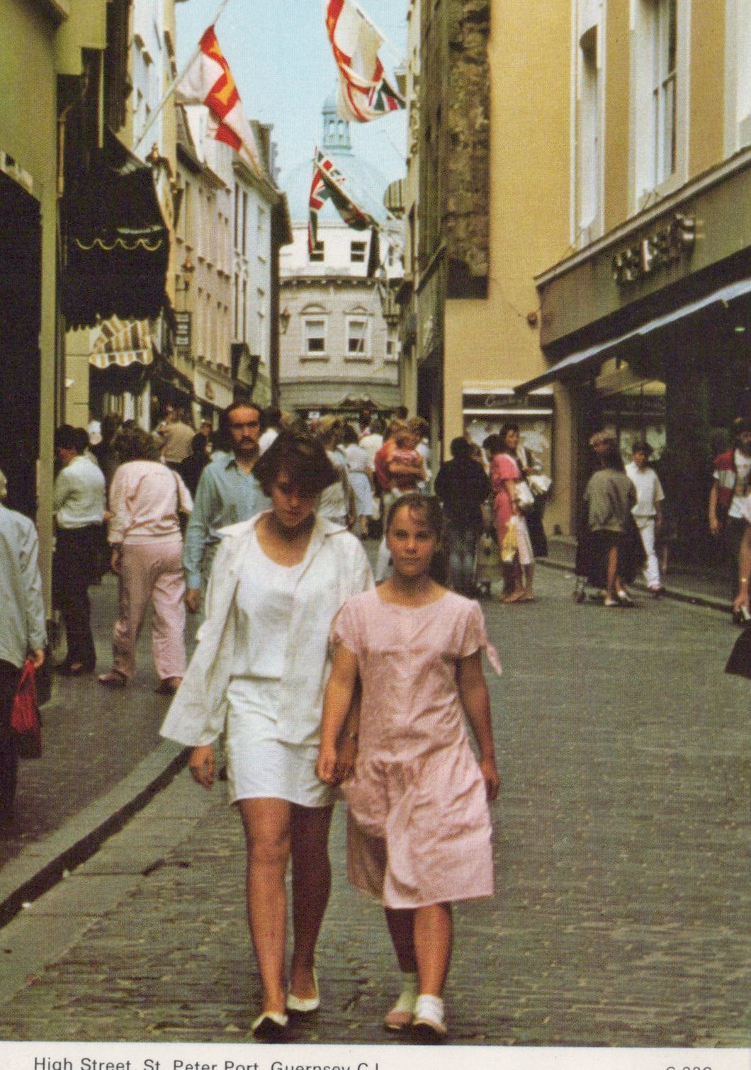 Two women walking down a busy street with shops and people in the background.