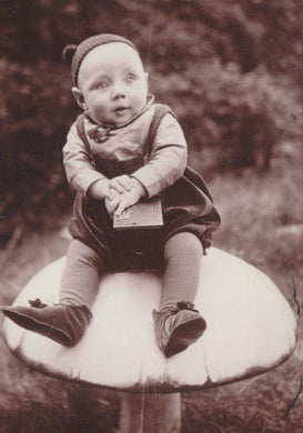 Vintage black and white photo of a child sitting on a mushroom-shaped object outdoors.
