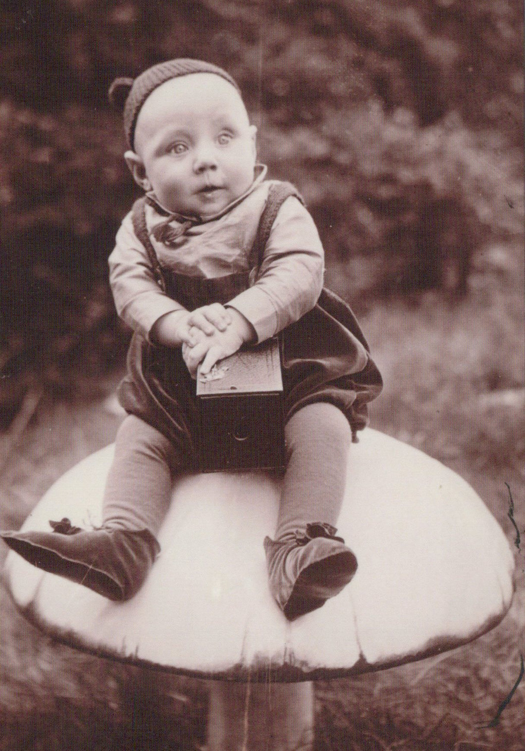 Vintage black and white photo of a child sitting on a mushroom-shaped object outdoors.