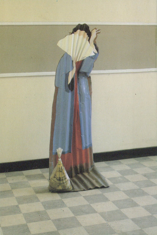 Person in a long, colorful dress holding a fan in a room with a checkered floor.
