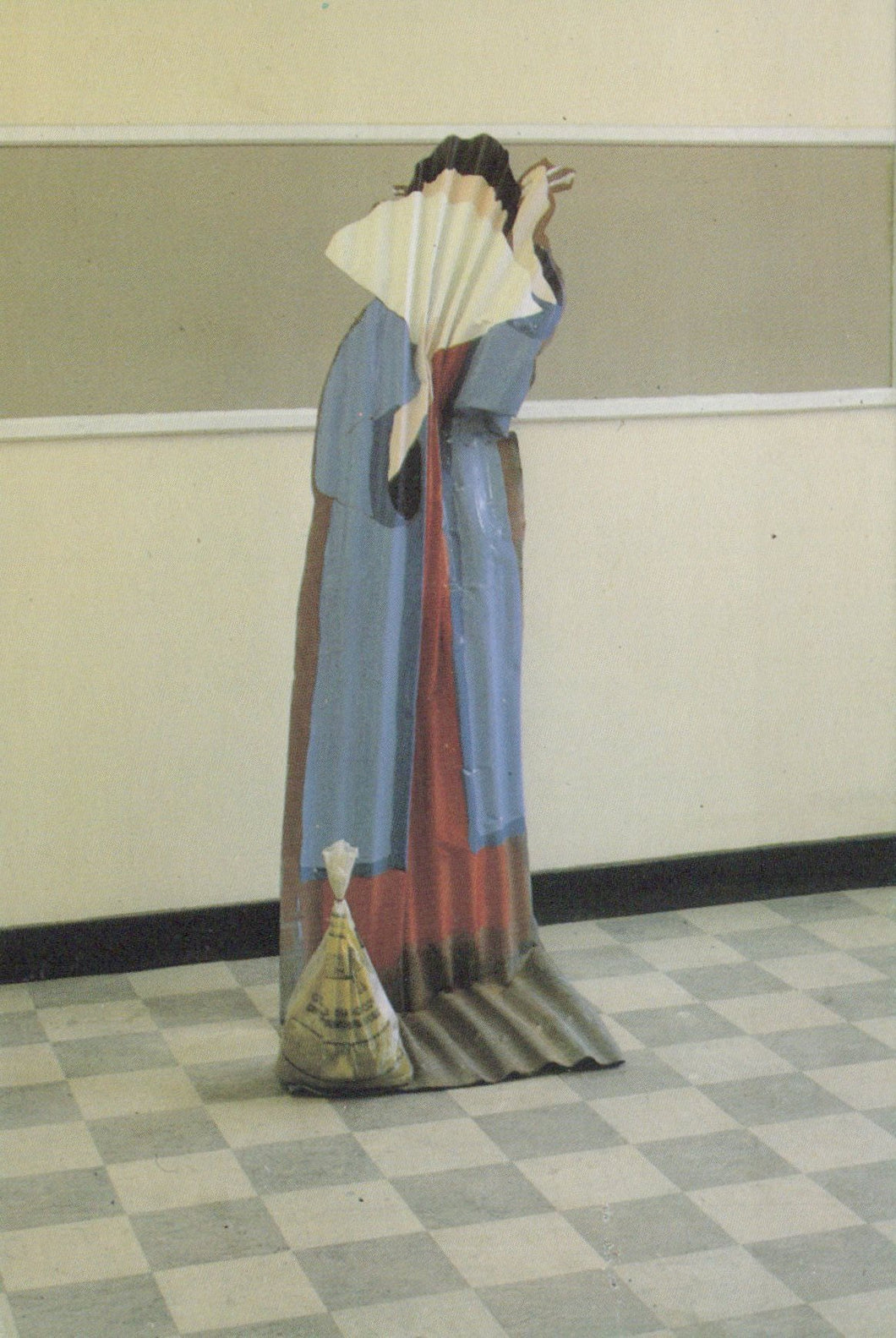 Person in a long, colorful dress holding a fan in a room with a checkered floor.