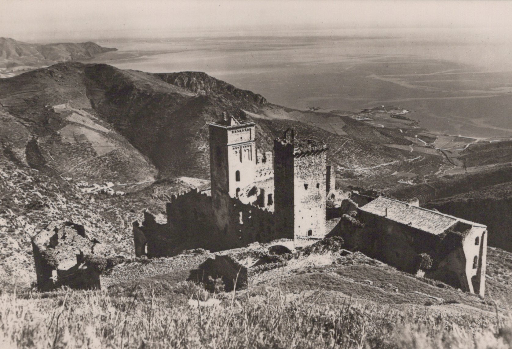 Vintage black and white photograph of a castle on a hill with a vast landscape in the background.