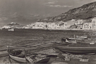 Black and white photograph of a coastal scene with boats and buildings.