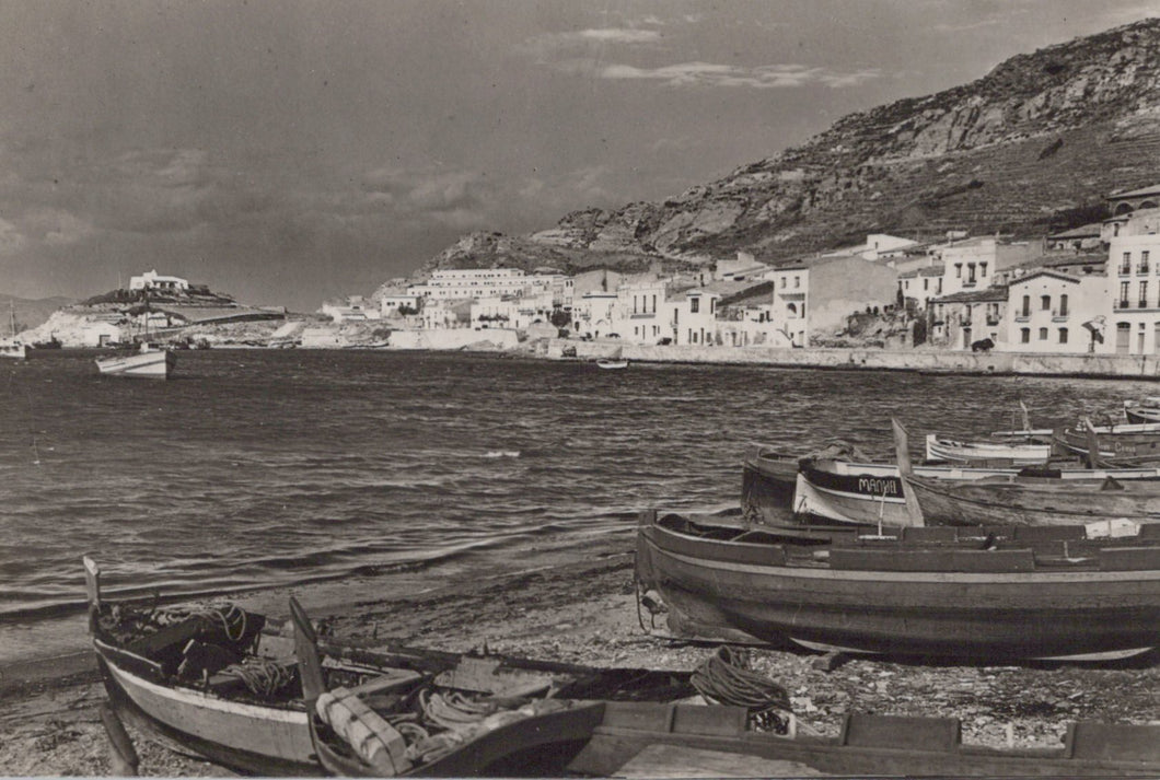 Black and white photograph of a coastal scene with boats and buildings.