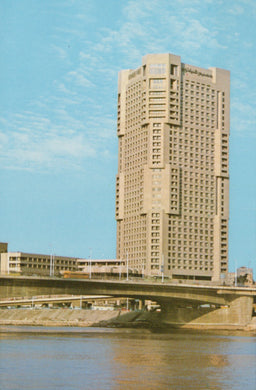 Tall beige building with a blue sky and water reflection
