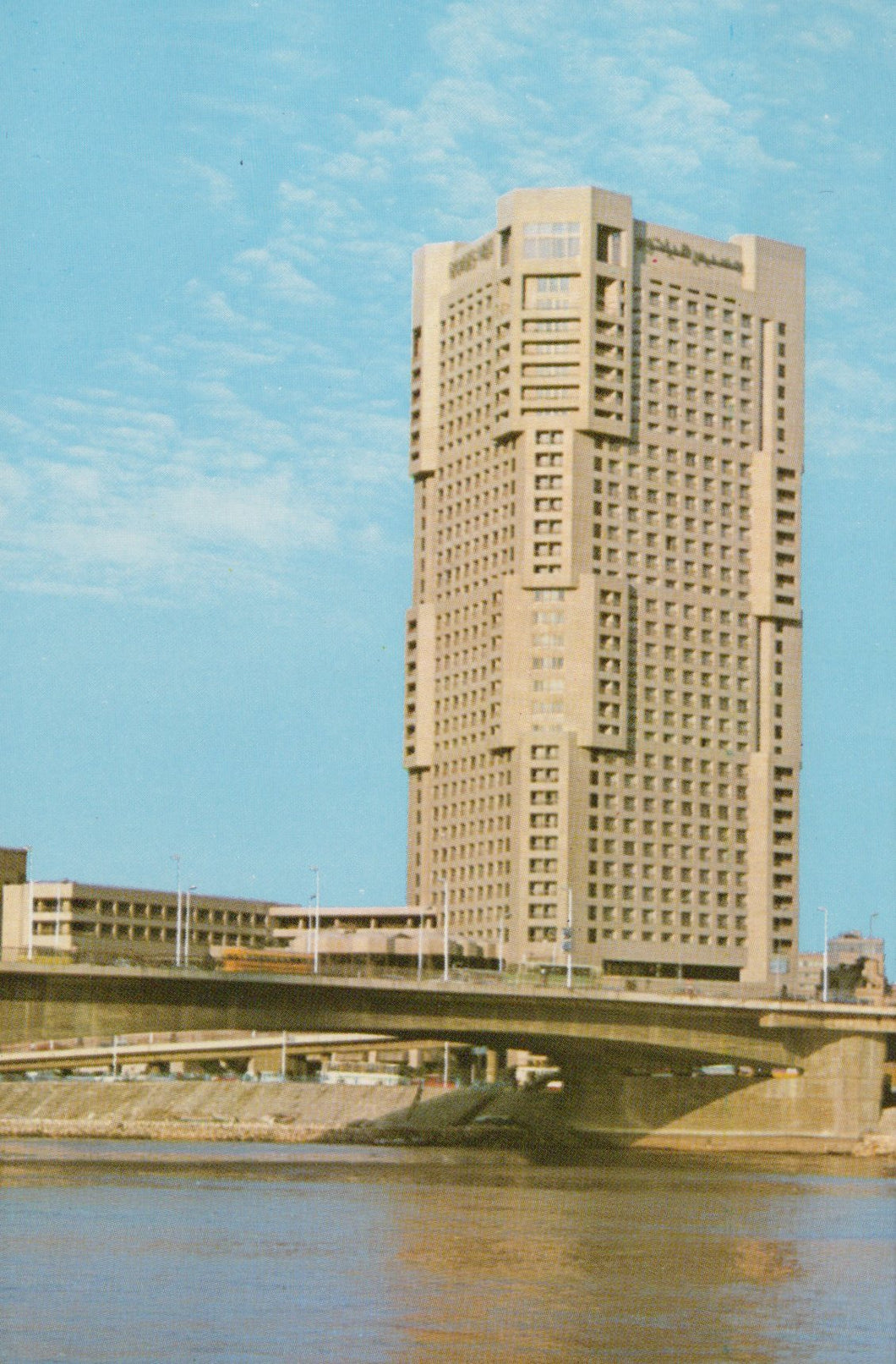 Tall beige building with a blue sky and water reflection