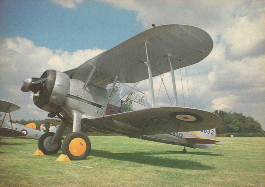 Vintage biplane on a grassy field with a blue sky and clouds in the background