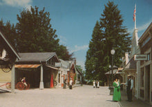 Load image into Gallery viewer, Vintage-style street scene with people and buildings under a clear blue sky.
