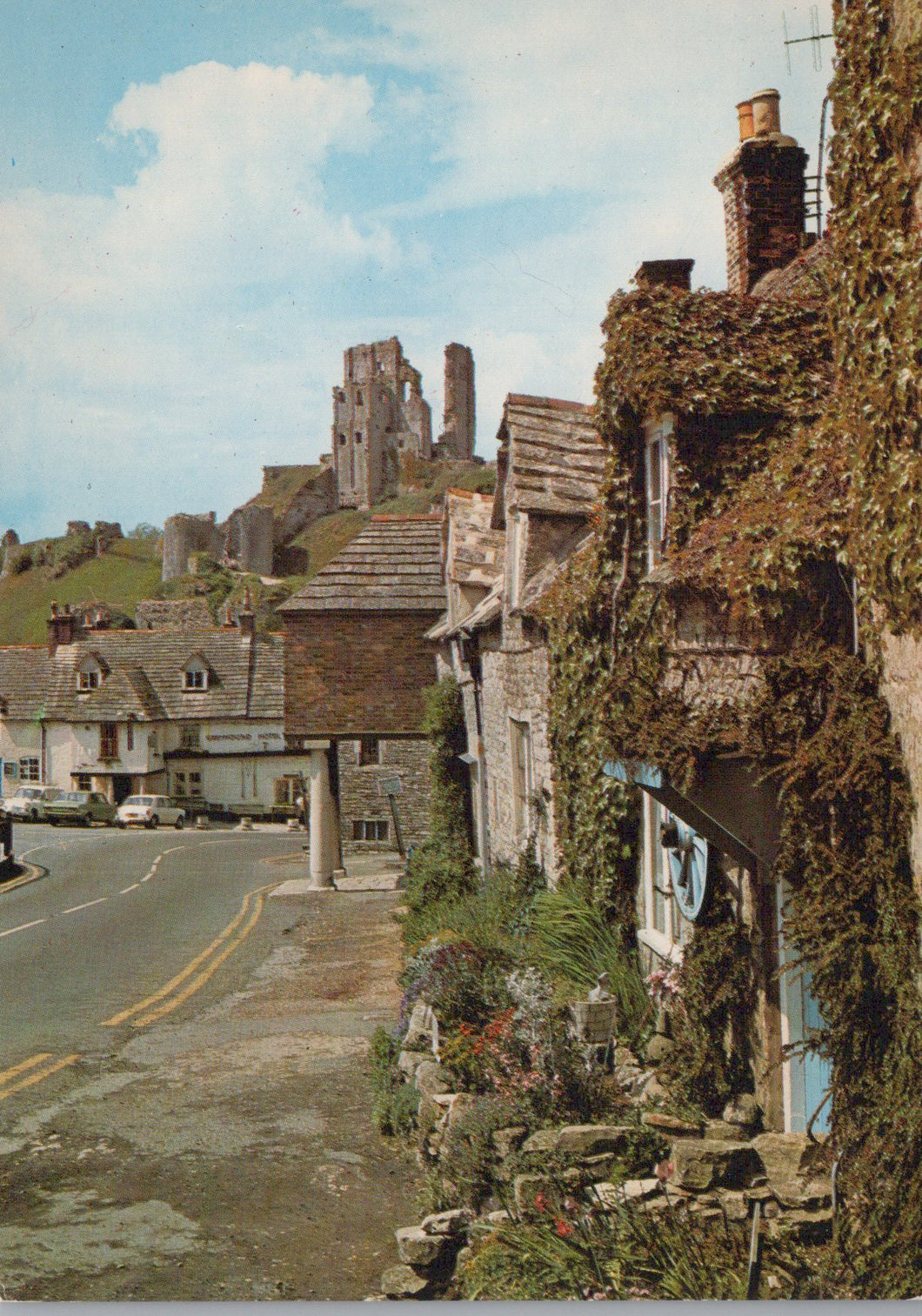 Village street with old stone houses and Corfe Castle ruins in the background.