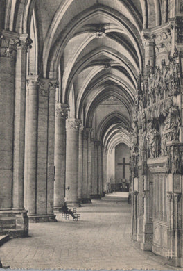 Narrow stone hallway with high vaulted ceilings and decorative columns, leading to a cross.
