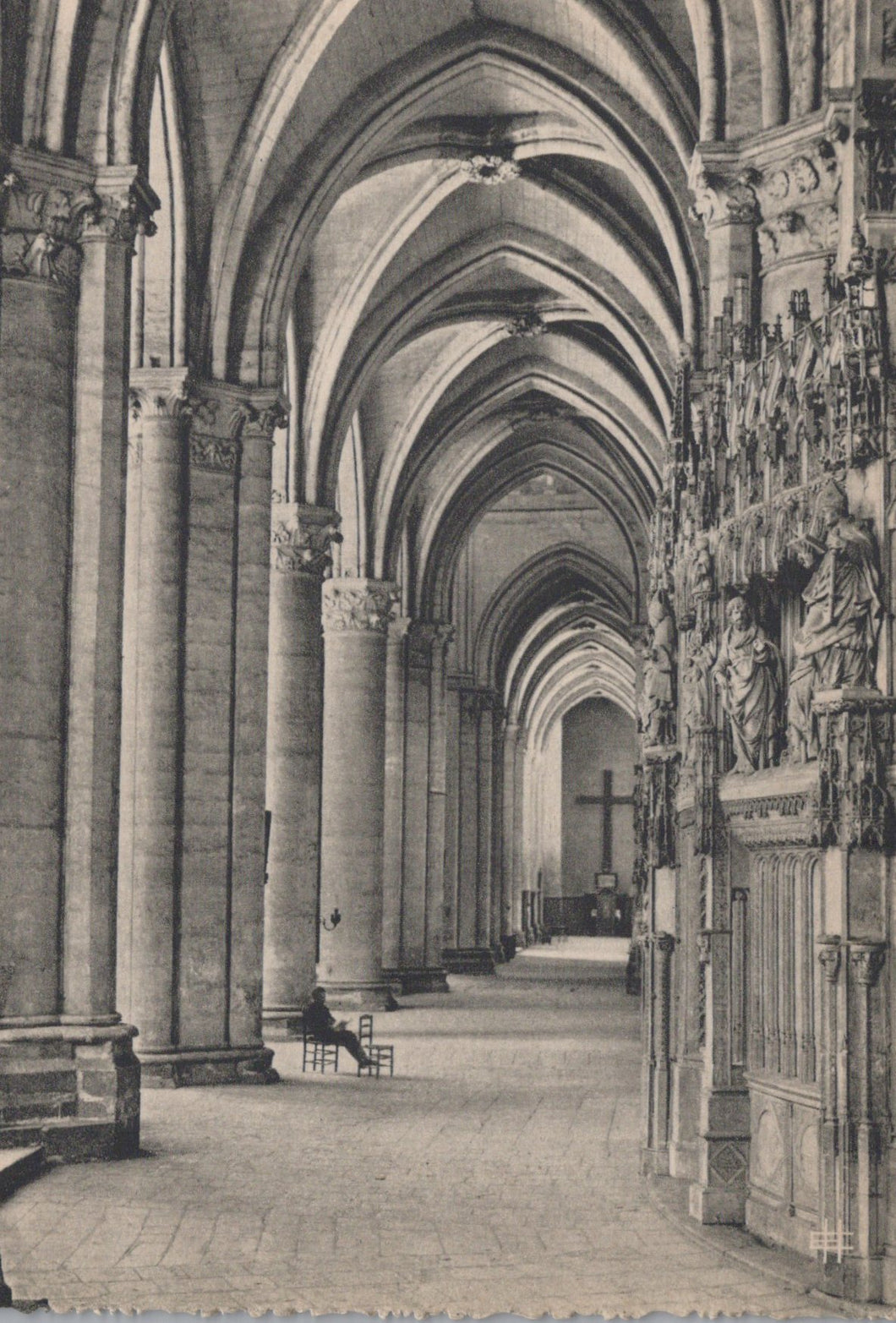 Narrow stone hallway with high vaulted ceilings and decorative columns, leading to a cross.