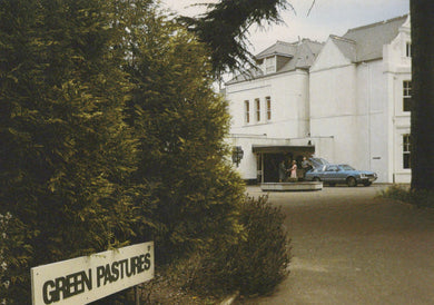 White building with 'Green Pastures' sign in front, surrounded by trees.