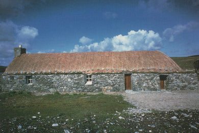 Stone building with a thatched roof under a blue sky with clouds