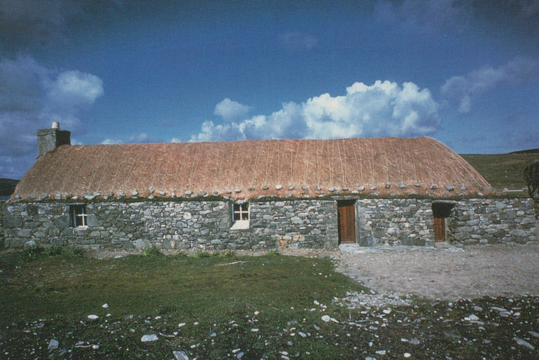 Stone building with a thatched roof under a blue sky with clouds
