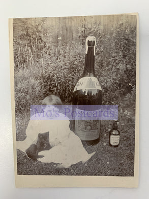 Vintage-style photo of a person sitting outdoors with a large bottle and smaller bottle, overlaid with 'Mo's Postcards' text.