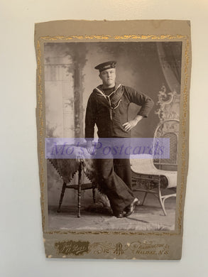 Vintage photo of a person in a sailor suit with decorative frame and watermark.