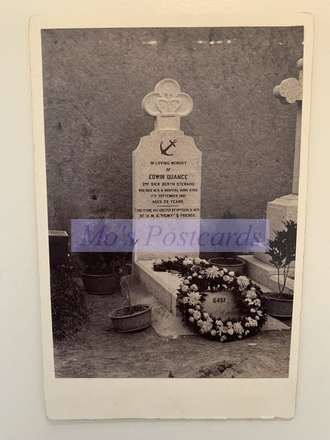 Grave with headstone and wreath in a cemetery, featuring 'Mo's Postcards' watermark.