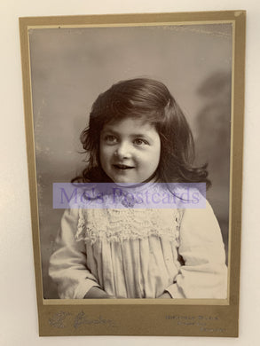 Vintage black and white photo of a young girl with a smile, framed by a gold border.