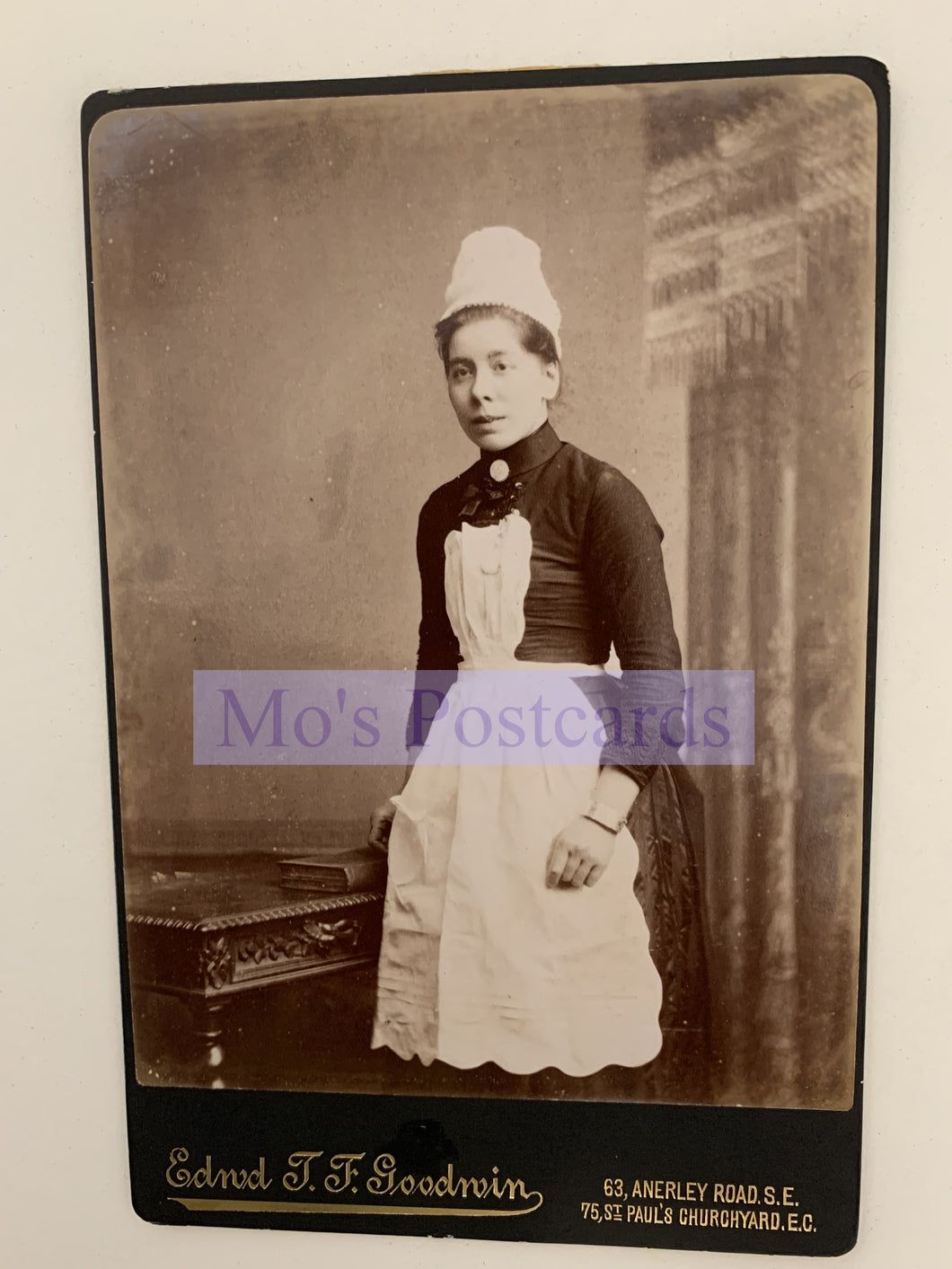Vintage black and white photograph of a woman in a maid's uniform with a blurred background.