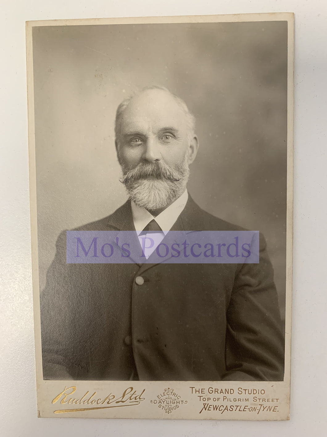 Vintage black and white portrait of a man with a beard, framed by 'Mo's Postcards'.
