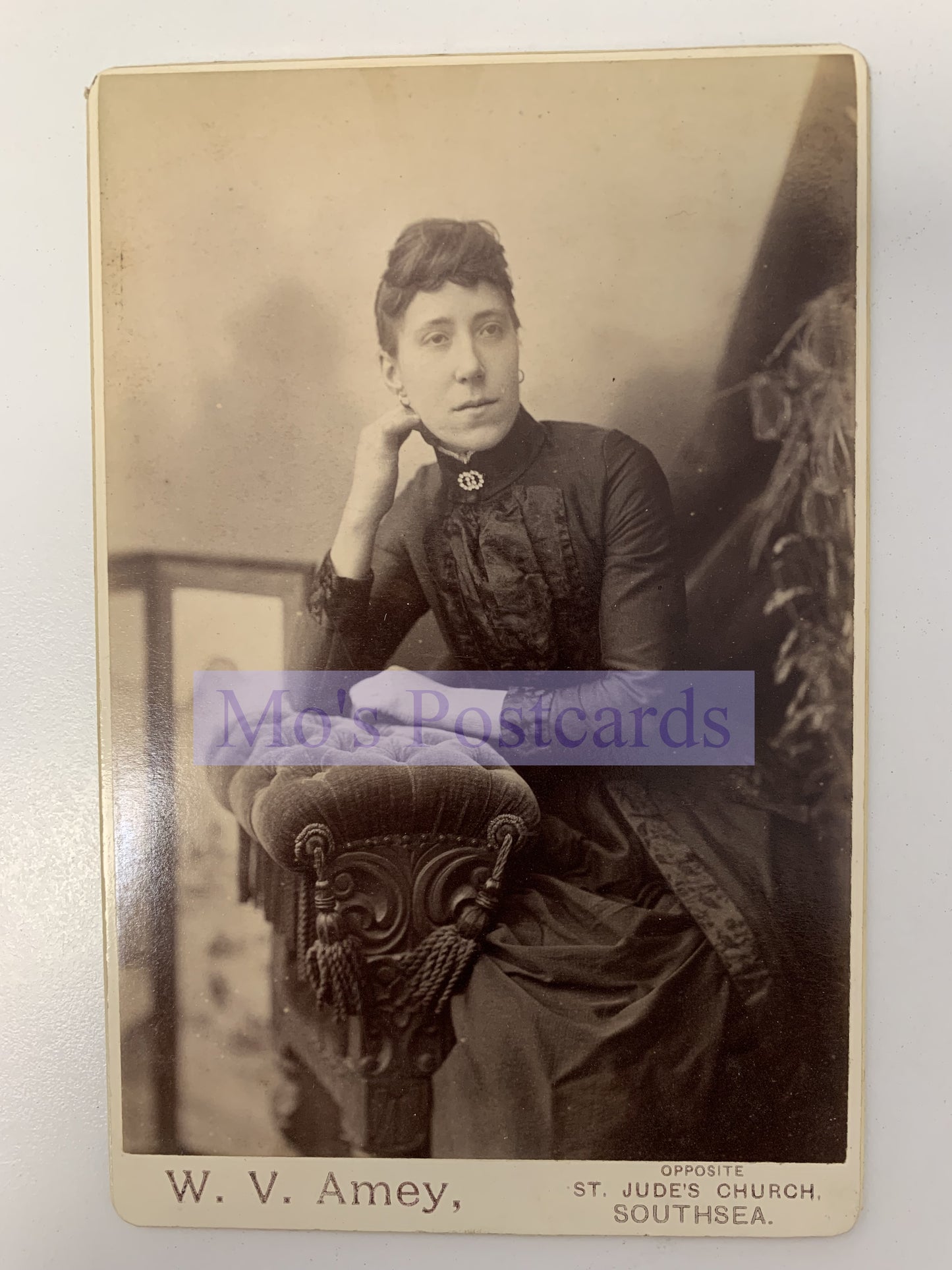 Vintage photograph of a woman sitting on a decorative chair with 'W. V. Amey' branding.